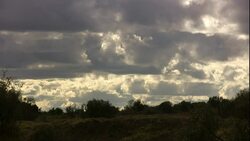 Stormy clouds linger in the sky over a shrub-covered hill. Stock Footage