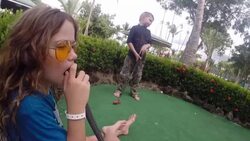 Close up of girl with yellow sunglasses holding golf club and father and son getting ready to take next shot at mini golf at resort. Stock Footage
