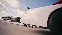 Pit-crew rolls jack out from under race-car, driver speeds off, pit-crew celebrates Stock Footage