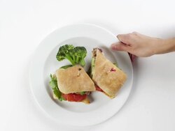 CU Woman hand entering setting down round white plate with sandwich sliced in two pieces and broccoli on the side / Omaha, Nebraska, United States Stock Footage