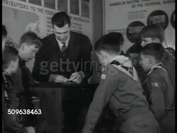 1941: PROTECTING DEFENSE INDUSTRY: Man walking out of safe w/ papers, guard closing doors. TEACHING SCOUTS: FBI Field Agent showing Boy Scouts in uniform fingerprinting. (VO mentions fighting the fifth column) Instructional Video