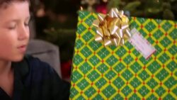 Curious young boy shakes present intently in front of Christmas tree Stock Footage