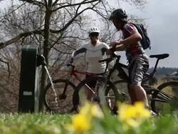 Bicycling couple arrive at water fountain, woman tosses water Stock Footage