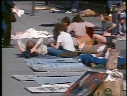 1972 zoom out hippies lying + sitting on ground + holding posters on Washington DC street / peace sign Stock Footage