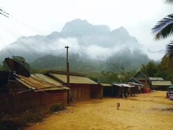 WS Shot of small village street in front side with primitive structures dog looking at towards and woman throwing water from bucket with mountain and clouds in back side / Village near Muang Ngoi, Luang Prabang, Laos Stock Footage