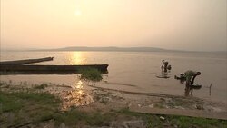 Women wash pots and pans on riverbank at dusk Stock Footage