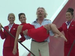 Sir Richard Branson carries singer Sarah Harding on wing of jet flanked by airline staff Stock Footage