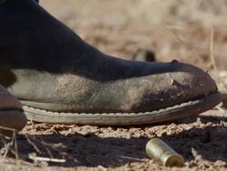 Up close view of cowboy boots as bullet shells fall to the ground next to them. Stock Footage