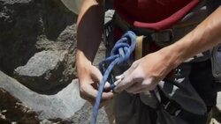 A young man using a figure eight follow-through knot to tie his rope to his harness while rock climbing. Stock Footage