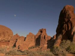 Red rock desert landscape at dusk with full moon in the empty blue sky -- pan Stock Footage