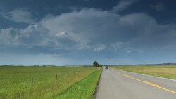 Car approaches on prairie road with storm in distance Stock Footage