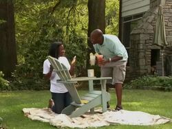 African American husband and wife painting wooden adirondack chair in yard Stock Footage