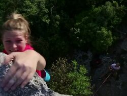 Young woman climbs steep rock wall above belayer Stock Footage