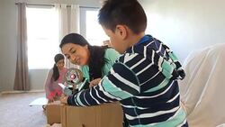 Mother helping young son tape cardboard boxes closed while packing belongings to move Stock Footage