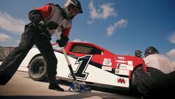 Pit-crew jacks race-car and removes lug-nuts and tire, man rolls new tire Stock Footage