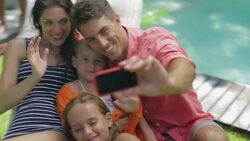 Family taking self-portrait on lounge chair at poolside Stock Footage
