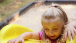 Young girl slides backwards on playground slide into sandbox while her brother watches Stock Footage