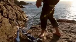 Man traverses highline stretched above sea below, then looks off Stock Footage