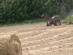 MS Tractor passing through grass field with bale of straw in field / Serrig, Rhineland-Palatinate, Germany Stock Footage