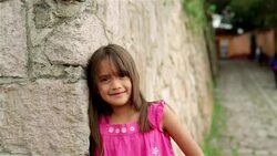 Cute young hispanic girl smiles at camera on third-world street corner, people walking in background (dolly-shot) Stock Footage