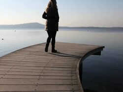Boom upwards as woman walks along lake wharf, takes picture Stock Footage