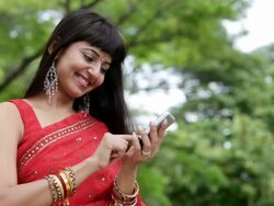 MS  Young woman in sari  messaging on mobile phone in park / Singpore Stock Footage