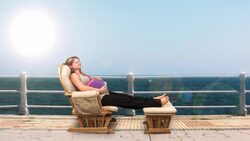 A pregnant woman relaxes in a glider against a computer generated seaside resort. Stock Footage