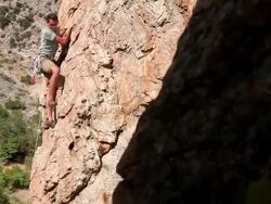 Handheld tracking shot of a rock-climber struggling his way up a cliff. Stock Footage