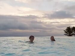 Wide shot boy and girl jumping into infinity pool / medium shot swimming toward CAM / smiling at CAM / South Africa Stock Footage
