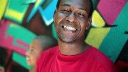 Brazilian father with children smiles at camera leaning on graffitied wall in Rio Stock Footage