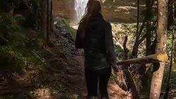 Young female athlete running through the woods towards a waterfall Stock Footage