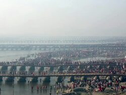Milling crowds of pilgims wade across shallow river, bathe, or cross on pontoon bridges early in the morning, Kumbh Mela, India Stock Footage