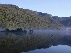 Mist rolls across forested mountain lake at dawn Stock Footage