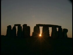 T/L Dusk and Stonehenge - orange starburst sun between stones, stones and moving people silhouetted Stock Footage