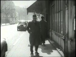 A man in a trench coat glances over his shoulder before entering a building. News Clip