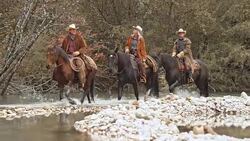 DS Two cowboys and cowgirl riding horses across river Stock Footage