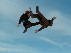 Wide shot two business men in midair after jumping on trampoline, with one nearly kicking other's head in midair / one man bounces back up Stock Footage