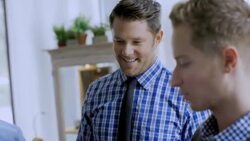 Young man admires shirt from Sale rack, friendly store manager offers advice and assistance Stock Footage