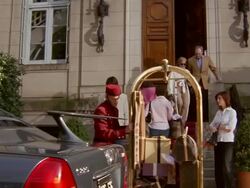 Tilt down wide shot wealthy man and woman leaving hotel + getting into limousine / bellman loading luggage Stock Footage