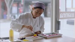 Pastry chef uses tweezers and squeeze bottle to decorate cake in storefront window Stock Footage