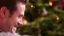 Father laughs as son tears into present in front of Christmas tree Stock Footage