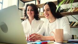 Two beautiful girls with laptop happily dancing sitting at the table Stock Footage