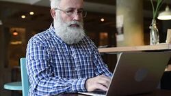 Adult senior man sitting with a laptop  smiles affably. Stock Footage