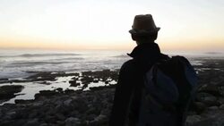 Solo Traveler on rocky coastline at sunset Stock Footage