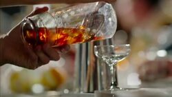 Bartender carefully pours mixed drink through strainer into cocktail glass Stock Footage