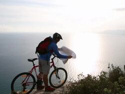 Mountain biker on cliff above sea, looks at map  Stock Footage