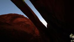 Looking up at the blue sky and sun through a red-rock mountain arch in the desert in Utah  (tilt) Stock Footage