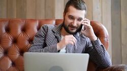 young adult man talking on the phone and looking at laptop Stock Footage