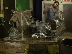 An artist chisels an ice sculpture while a worker drops blocks of ice into a storage can. Stock Footage
