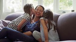 Daughter (Offspring)s kissing mother's cheeks on sofa Stock Footage